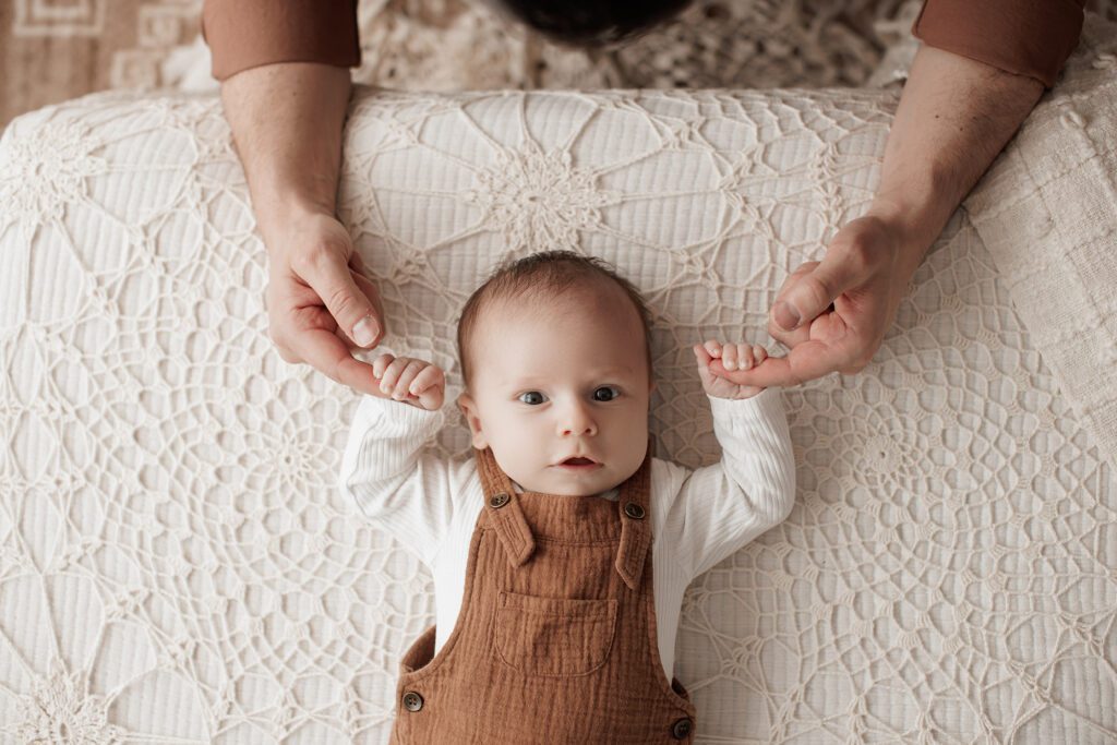 Is my baby too old for newborn photos - baby holding dad's hands on a bed