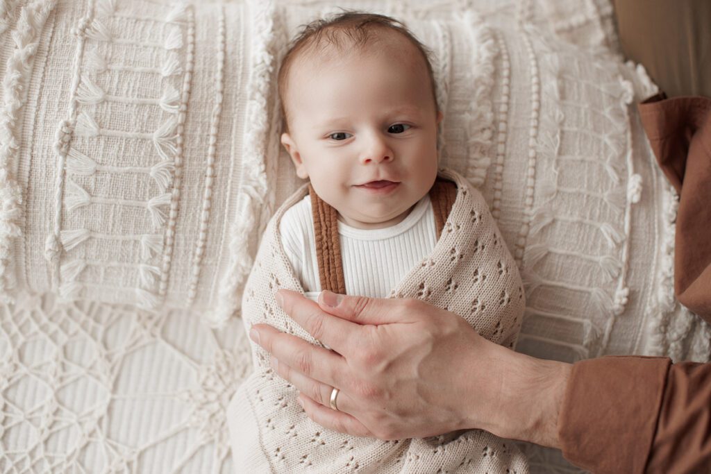 Is my baby too old for newborn photos - baby smiling while swaddled on a bed