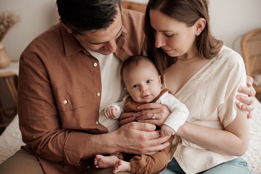 Is my baby too old for newborn photos - mom and dad sitting on a bed together with baby