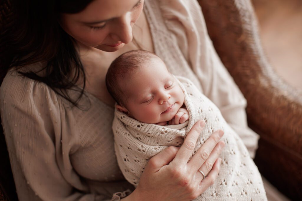 studio lifestyle newborn photography - mom sitting in a chair with her baby smiling in her arms