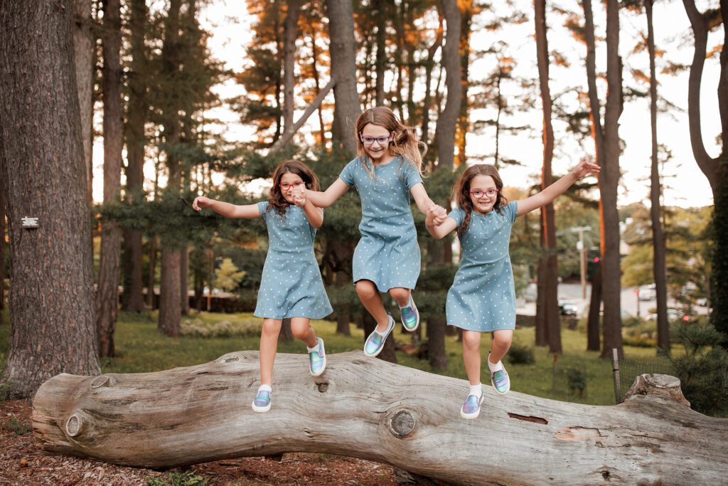 The best family photos location in Boston: The Arnold Arboretum - three girls jumping off a log in the woods during family photo session