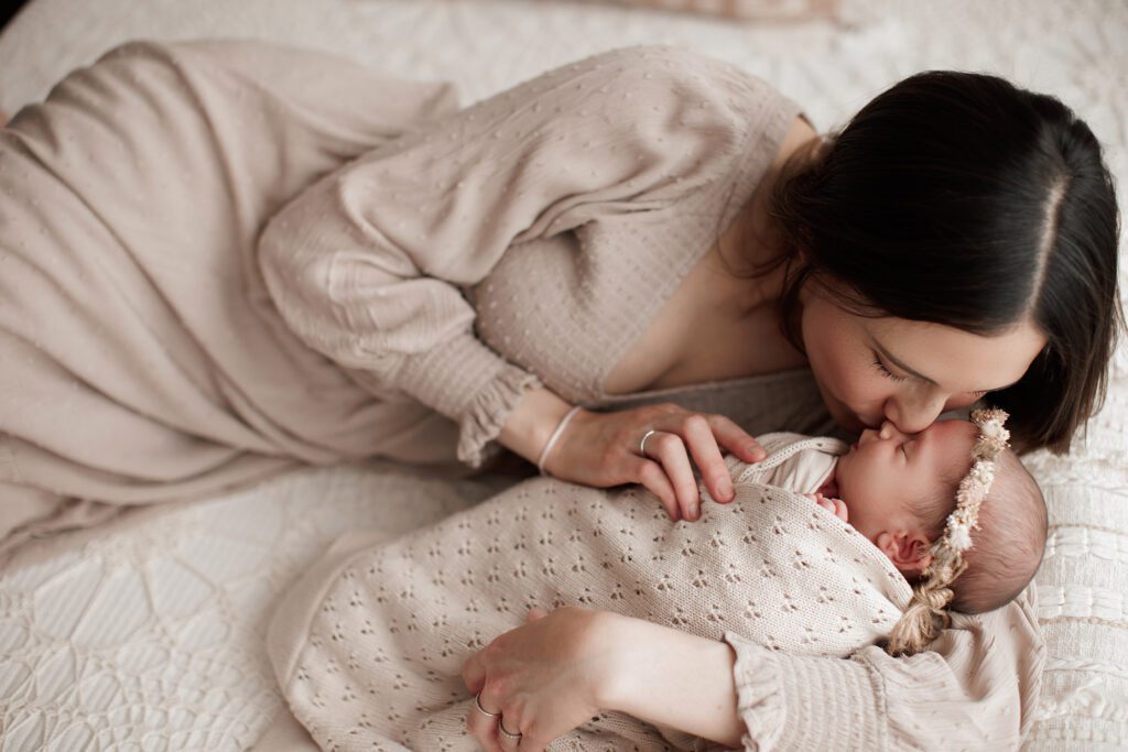 studio lifestyle newborn photography - mom laying with baby on a bed, kissing nose