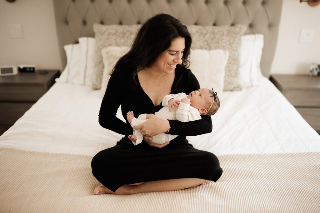 Which type of newborn photo session is best - baby girl in mom's arms on their bed in home lifestyle