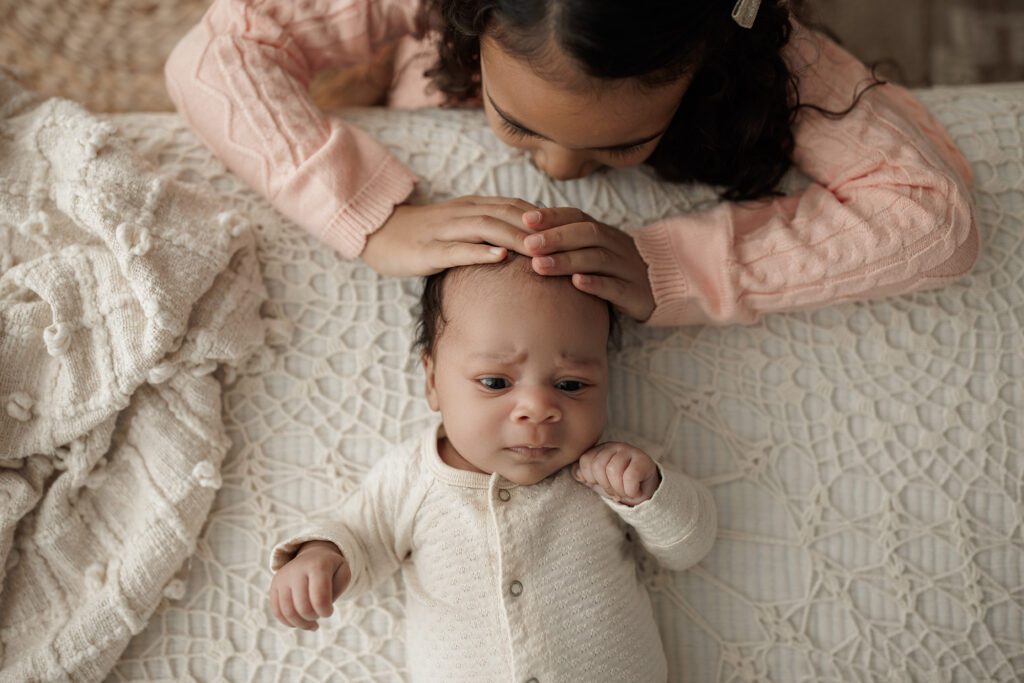 Opening your own photography studio - baby laying on bed and big sister giving kiss on the head