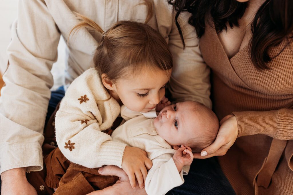 How old should my baby be for newborn photos? - family in home lifestyle newborn photos - big sister holding baby brother kissing his cheek, everyone in neutrals brown and cream