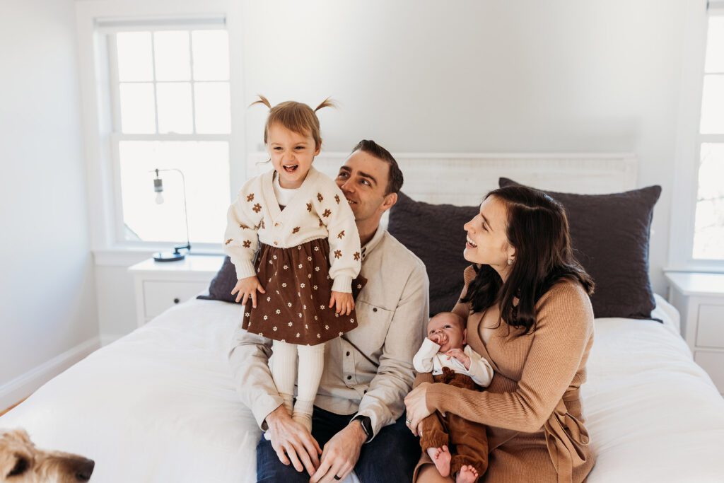 How old should my baby be for newborn photos? - family of four sitting on a bed