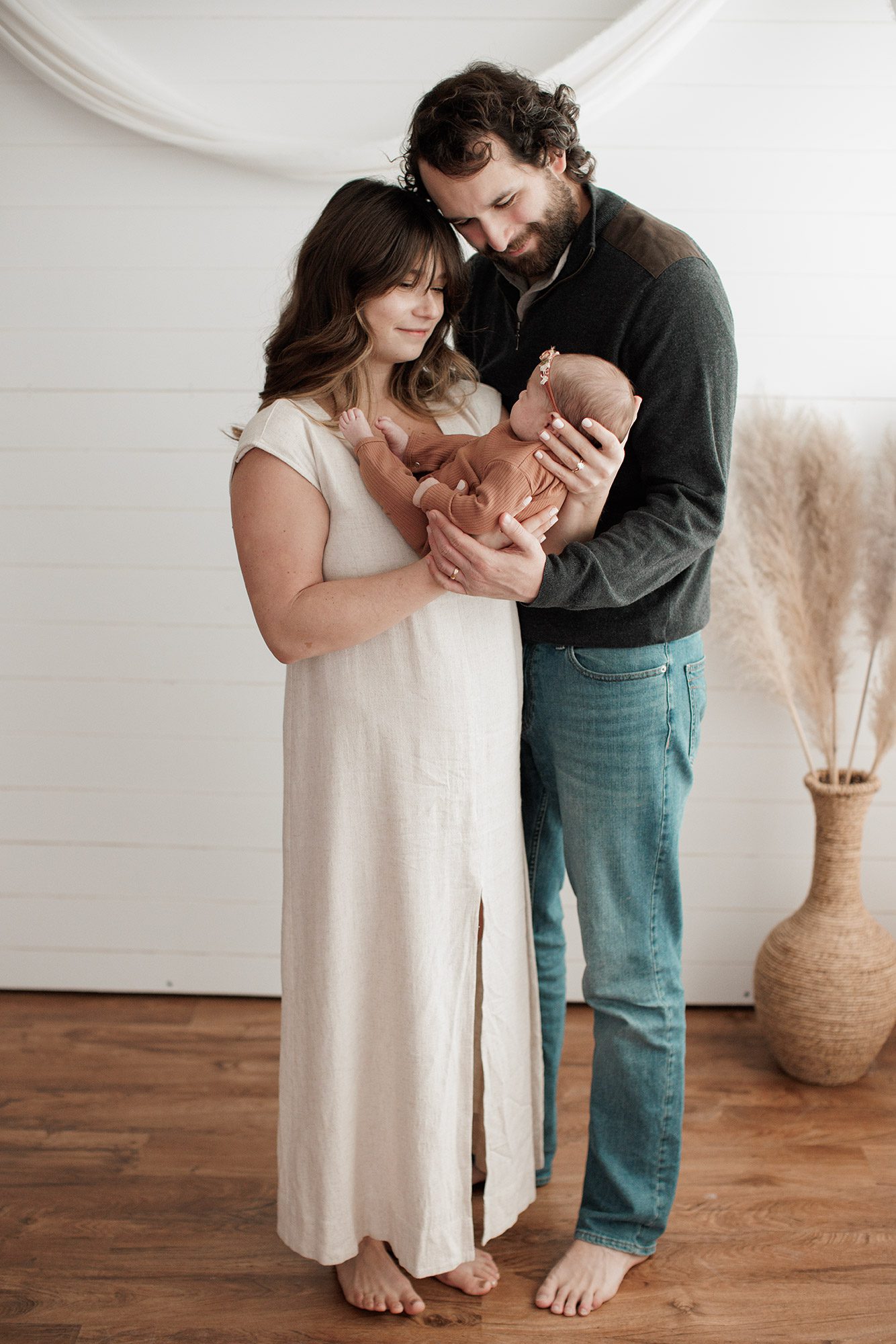 Favorite Newborn Photography Poses - parents holding baby girl in front of a white wall