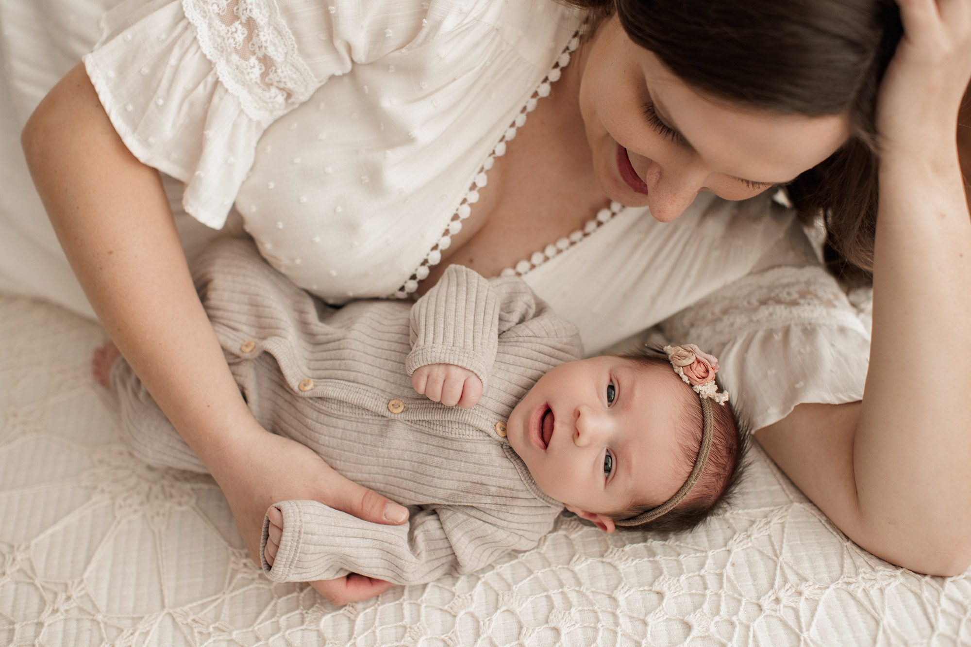 Best Location for a Newborn Photoshoot - mom and baby laying on a white bed in neutral outfits