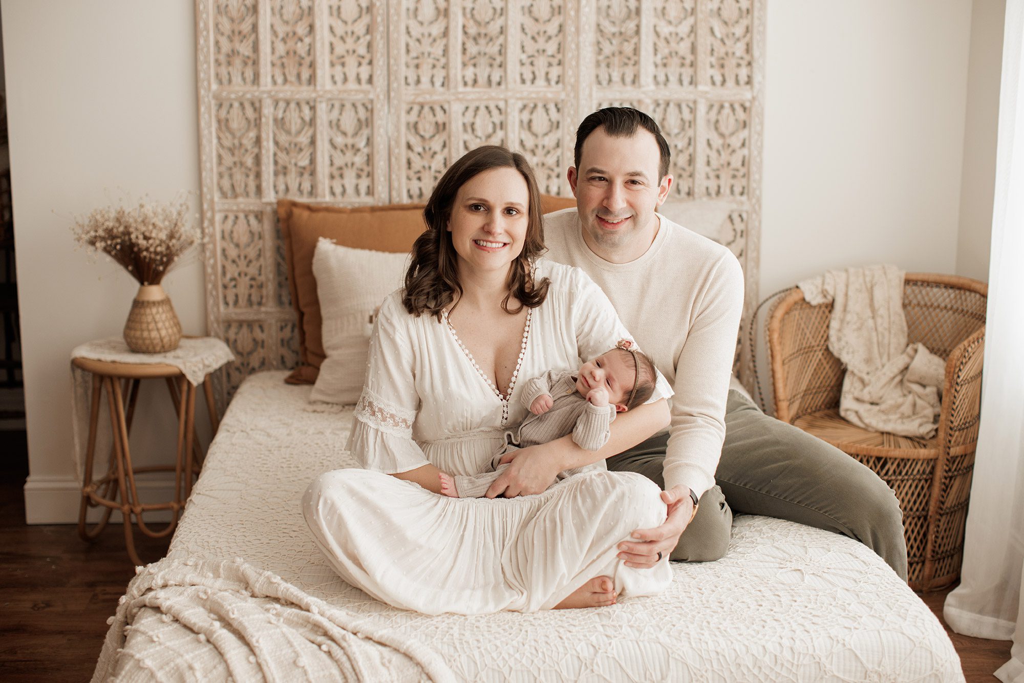 Best Location for a Newborn Photoshoot - mom and dad sitting on a bed with baby in their arms
