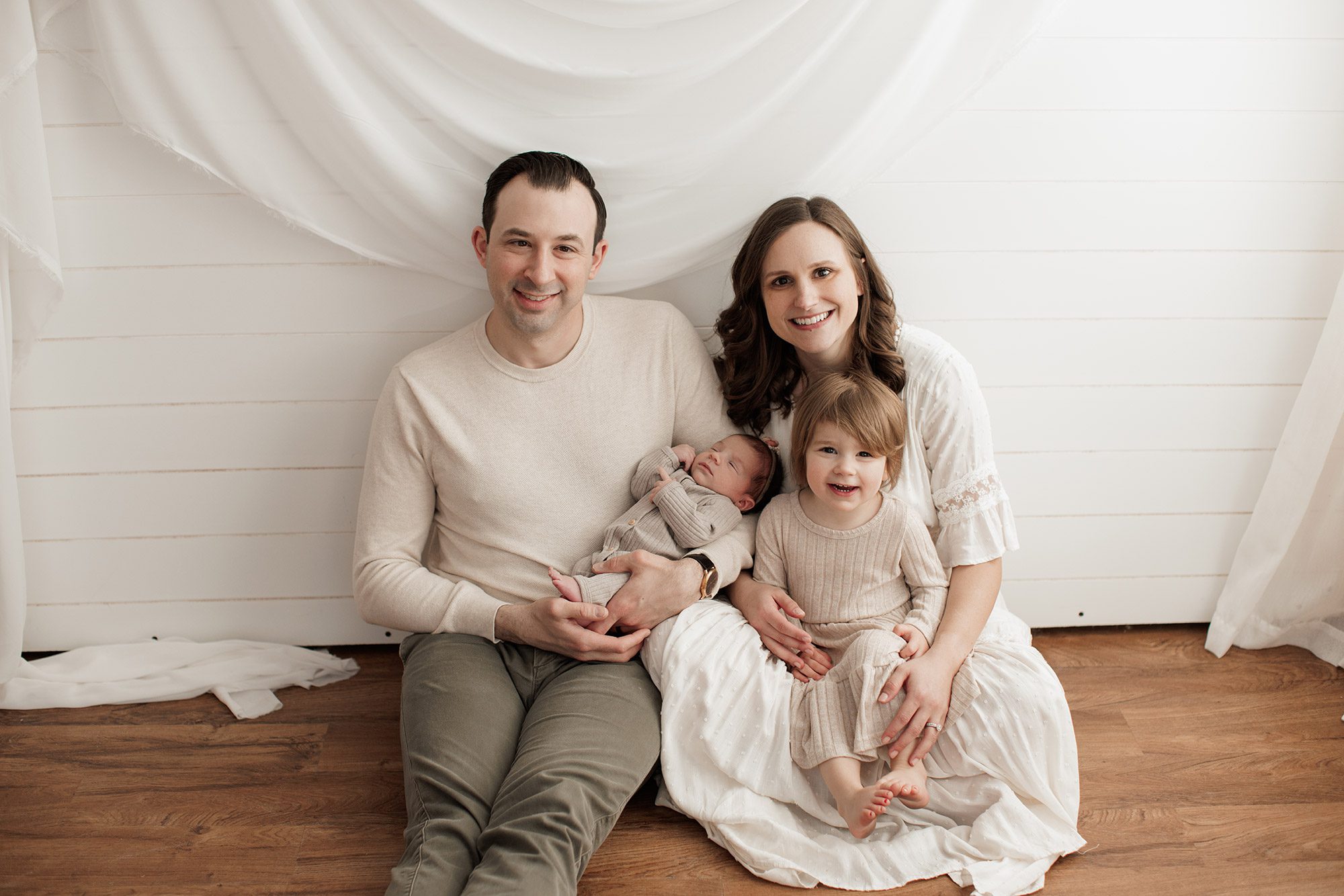 Best Location for a Newborn Photoshoot - family sitting on the floor looking at the camera and smiling