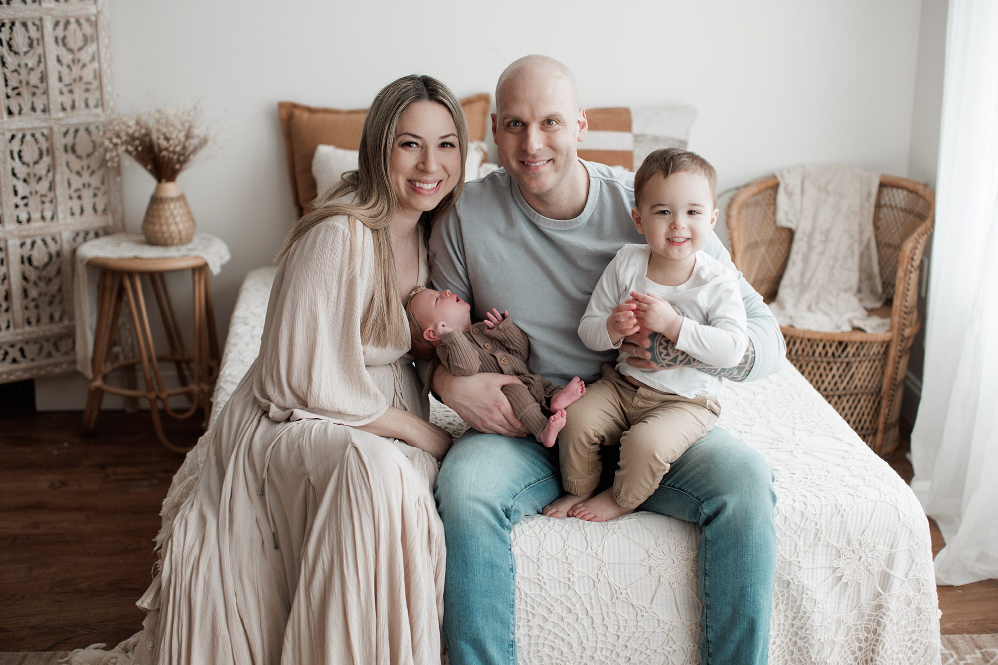 How to choose the right newborn photographer for your family - family of four sitting with new baby on a bed in a studio