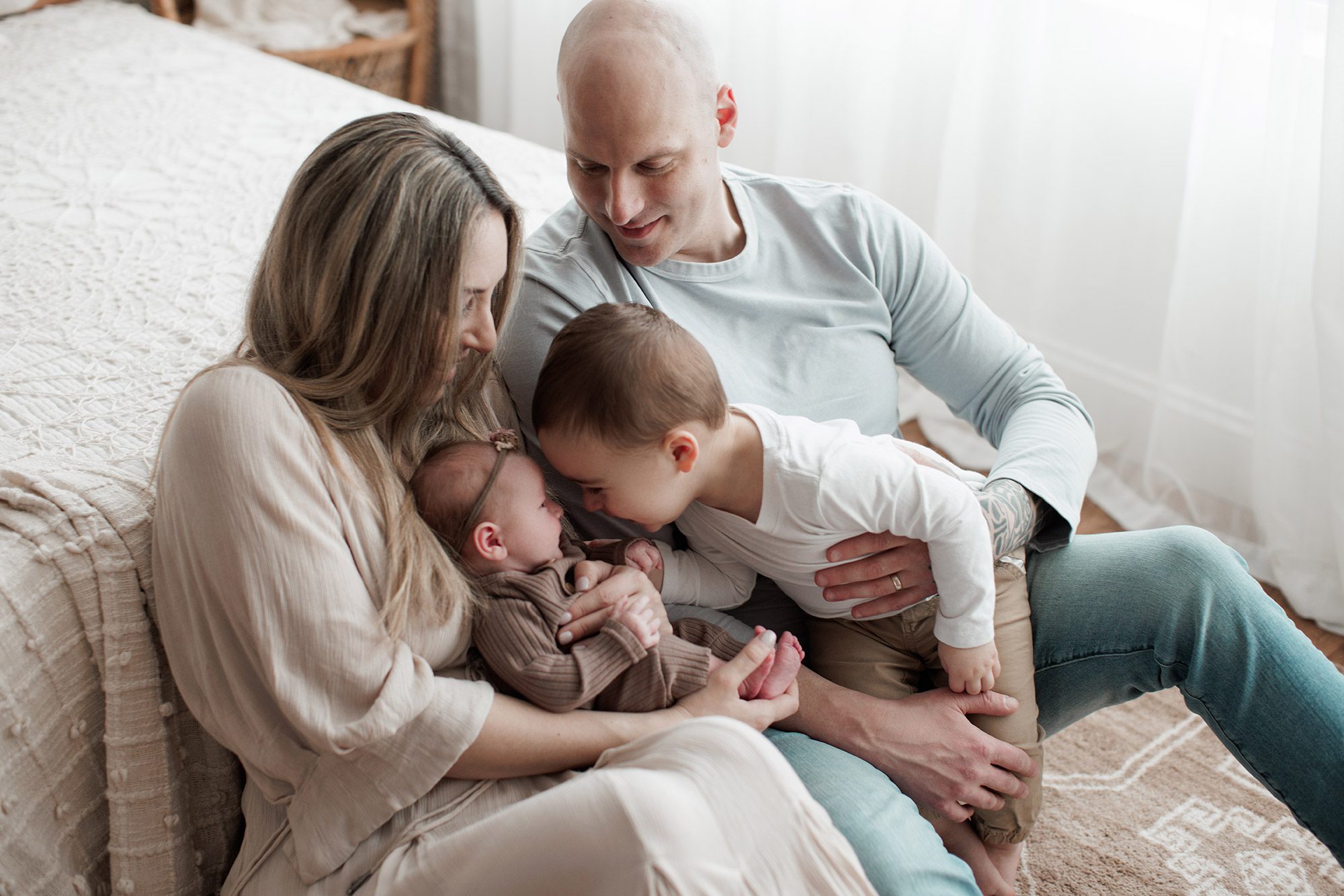 How to choose the right newborn photographer for your family - big brother with parents, kissing baby sister