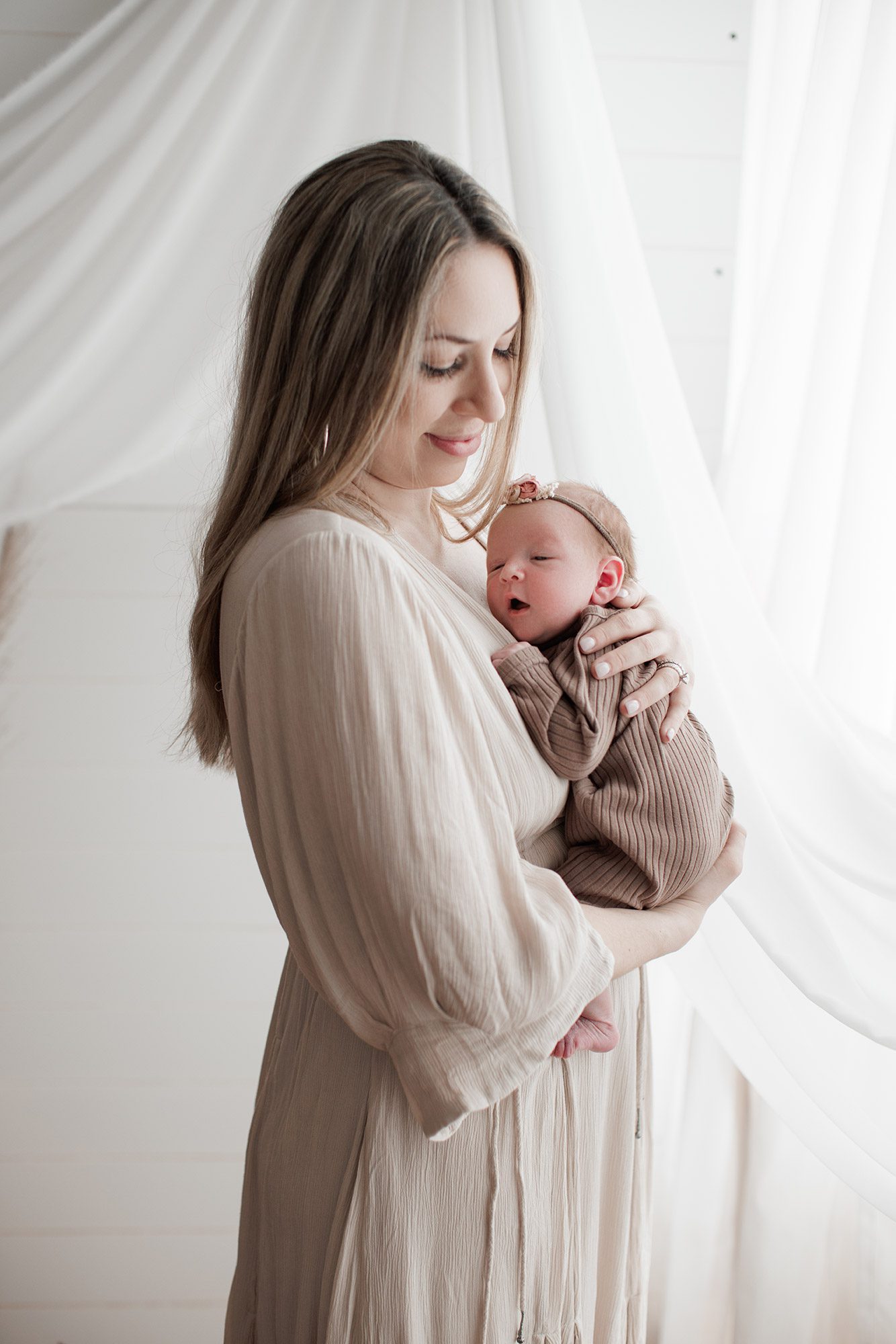 How to choose the right newborn photographer for your family - mom holding baby girl on her chest with a white background