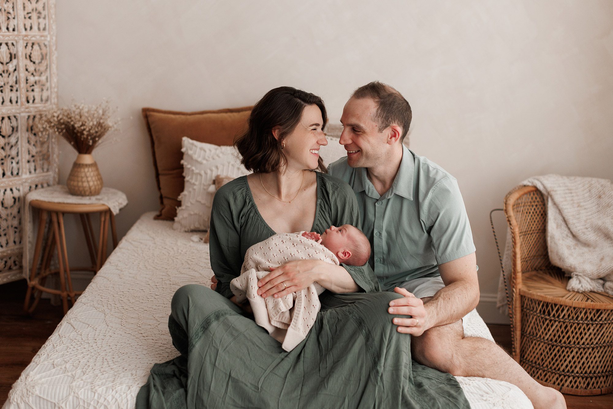 Rescheduling Your Photo Session for Illness - parents sitting together on a bed with a newborn baby